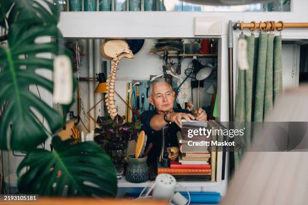senior male owner stacking books while working at antique shop - book shop stock pictures, royalty-free photos & images