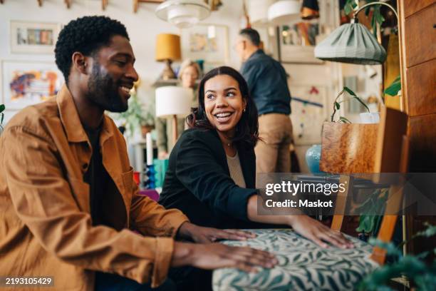 smiling female shop owner assisting male customer while buying chair at store - antique shop stock pictures, royalty-free photos & images