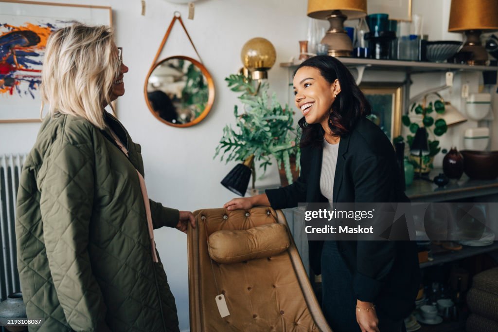 Happy female owner talking with customer buying furniture at antique store