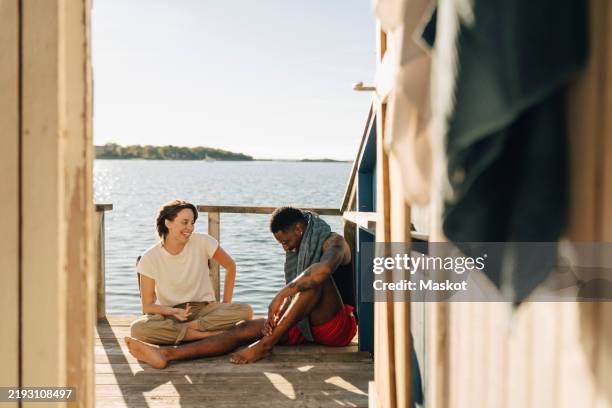 happy woman sitting on porch with male friend wearing towel at boathouse - vacation rental stock pictures, royalty-free photos & images