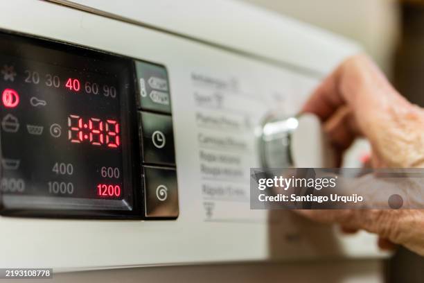 senior woman turning on the washing machine - wäsche stock-fotos und bilder