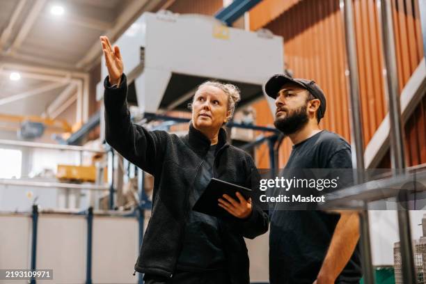 mature woman discussing with male coworker standing in distribution factory - 50 54 jahre stock-fotos und bilder