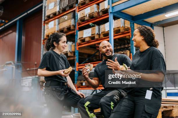 happy male and female warehouse workers eating burgers while enjoying and talking with each other in factory - entrepôt photos et images de collection