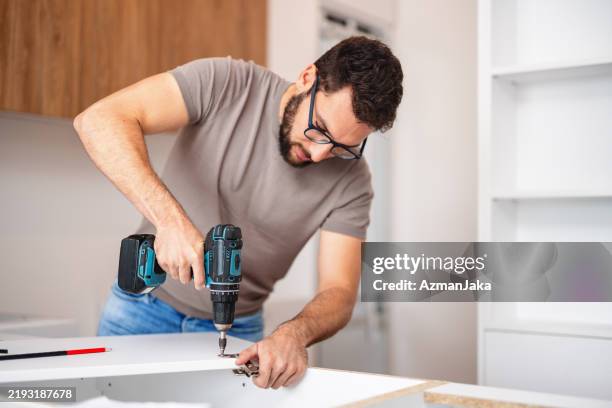 tischler montiert neuen küchenschrank in moderner wohnung - heimwerken stock-fotos und bilder