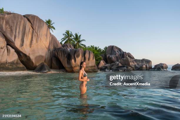 young woman wades into sea by rock boulders - escapism stock pictures, royalty-free photos & images