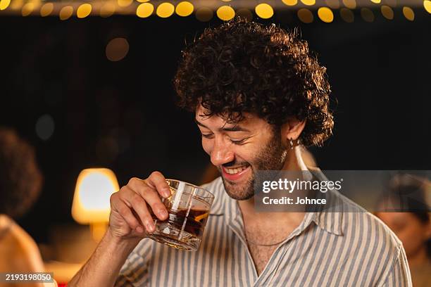 man smiling with drink at rooftop bar - whiskey tasting stock pictures, royalty-free photos & images
