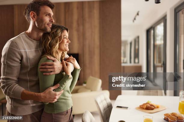 happy embraced couple day dreaming at home. - mid adult couple stock pictures, royalty-free photos & images