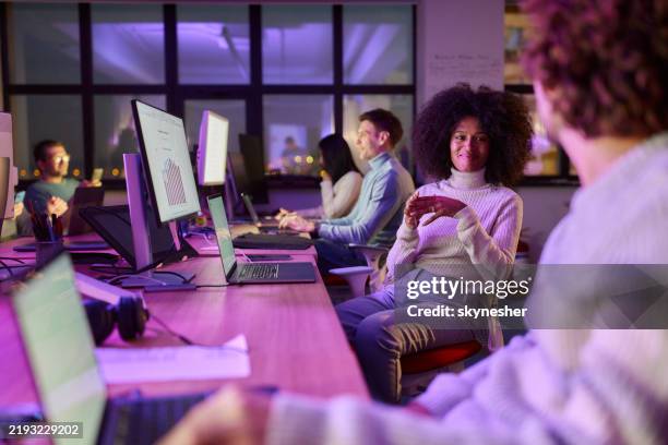 smiling black programmer talking to her colleague late in the office. - neon coloured stock pictures, royalty-free photos & images