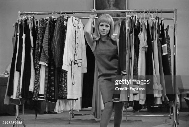 Fashion designer Prue Acton poses while holding the metal bar of a clothes rack, November 25th 1966.