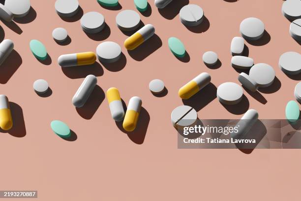 many pharmaceutical capsules and tablets scattered on a peach colored background with copy space. healthcare, medical treatment concept - bescherming tegen corona stockfoto's en -beelden