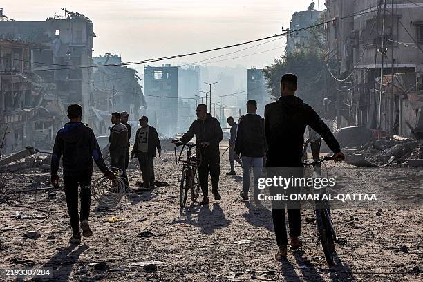 Men walk with bicycles through debris near the site of Israeli bombardment on a residential block in Jalaa Street in Gaza City on January 14, 2025...