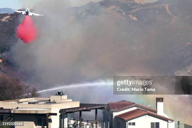 Firefighting aircraft drops the fire retardant Phos-Chek near homes during the Palisades Fire as wildfires cause damage and loss through Los Angeles...