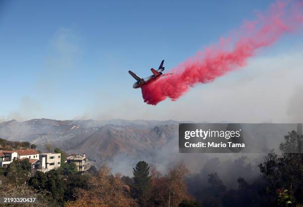 Firefighting aircraft drops the fire retardant Phos-Chek near homes during the Palisades Fire as wildfires cause damage and loss through Los Angeles...
