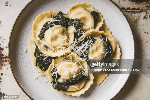 a plate of ravioli with spinach and cream sauce and shredded cheese - ravioli stock-fotos und bilder