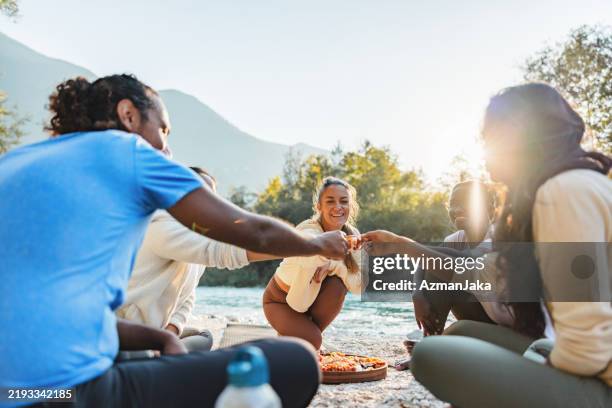 friends sharing food and laughter on a riverside picnic - riverbank stock pictures, royalty-free photos & images