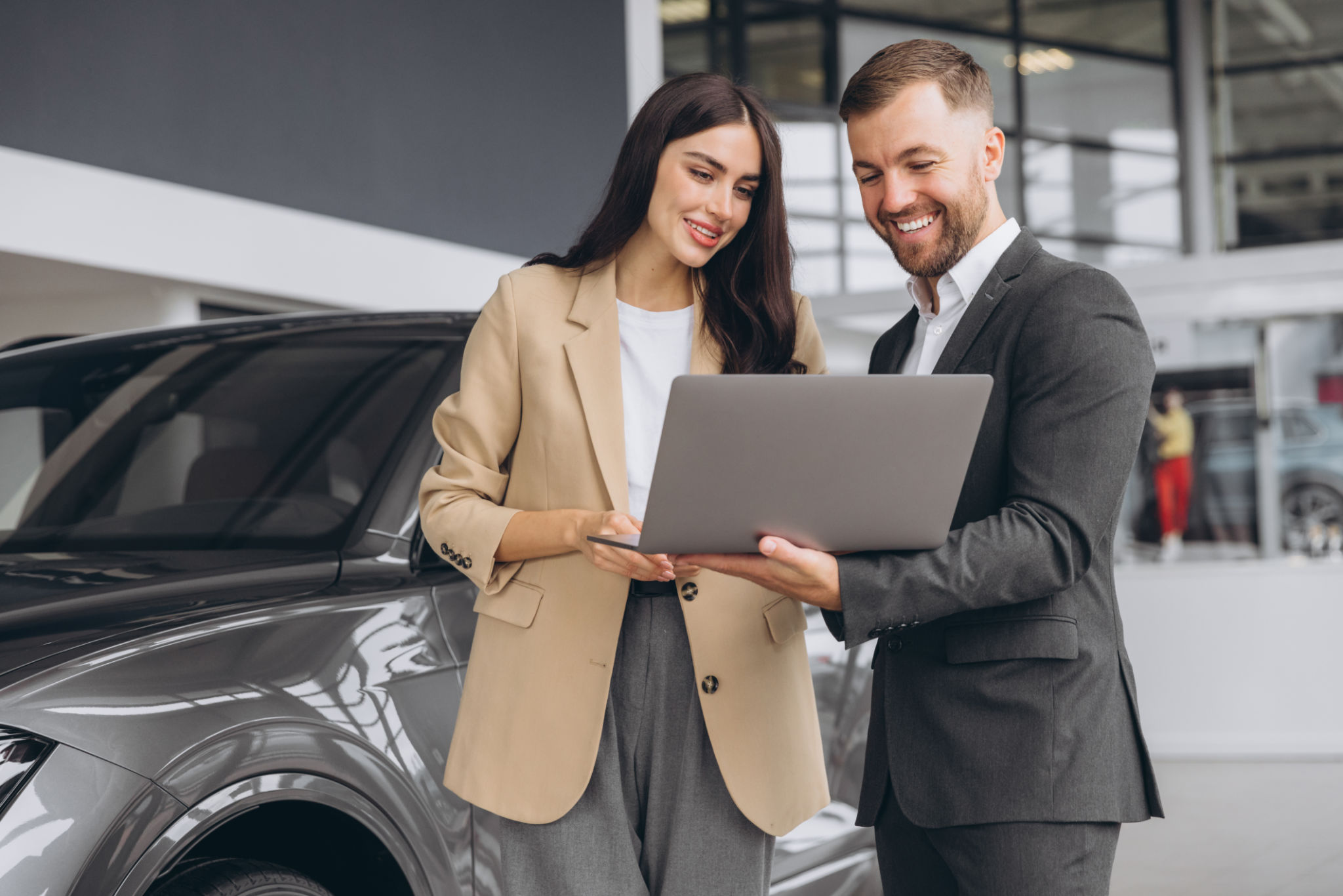 Male car salesman, recommends a car to a woman buyer, inspects cars in the showroom, the seller uses a laptop to view technical information on the car Male car salesman, recommends a car to a woman buyer, inspects cars in the showroom, the seller uses a laptop to view technical information on the car