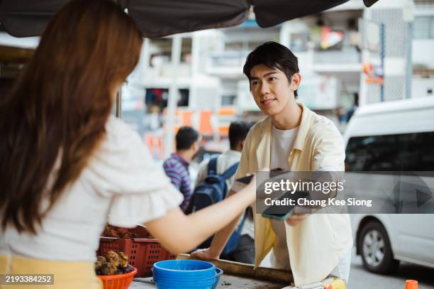 asian man receiving money from young woman by selling his fruit. - digital wallet stock pictures, royalty-free photos & images