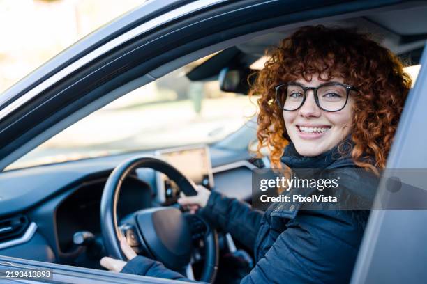 junge frau, die modernes auto fährt und in die kamera lächelt - privatfahrzeug stock-fotos und bilder