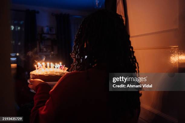 a woman walks into a dark room holding a cake covered in candles. - birthday candle stock pictures, royalty-free photos & images