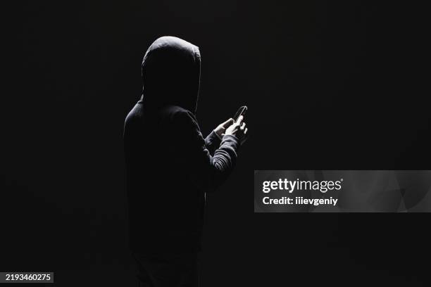 silhouette of man in hood with phone - verraad stockfoto's en -beelden