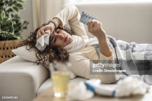 sick young woman lying on the couch holding a blister pack with antibiotics. - flu stock pictures, royalty-free photos & images