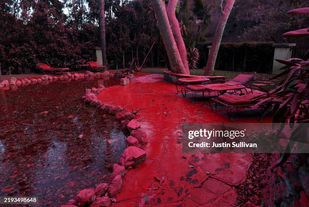Fire retardant covers a pool and lounge chairs after being dropped from a firefighting aircraft battling the Palisades Fire on January 11, 2025 in...