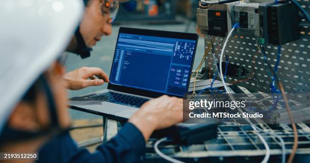 zwei junge ingenieure in der fabrik programmieren roboterausrüstung mit laptop und konzentrieren sich auf automatisierung und präzisionstechnologie. roboter-industriefabrik. - kette gebrauchsgegenstand stock-fotos und bilder
