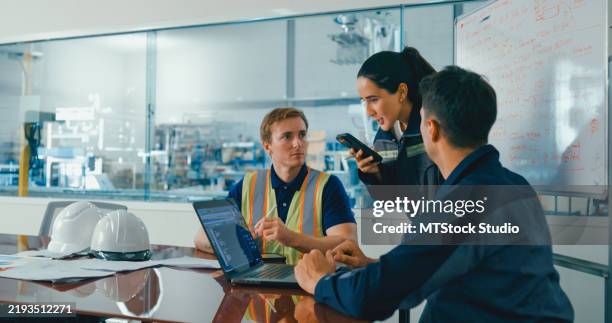 team of engineers in factory meeting, using laptop and uses translate language app on smartphone to discuss project details and strategies. robotic industrial factory. - vertaling stockfoto's en -beelden