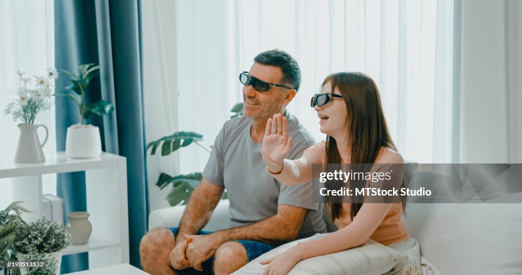 Mature father and daughter enjoy watching a 3D movie at home, wearing 3D glasses and sitting on the sofa. Family bonding and entertainment.