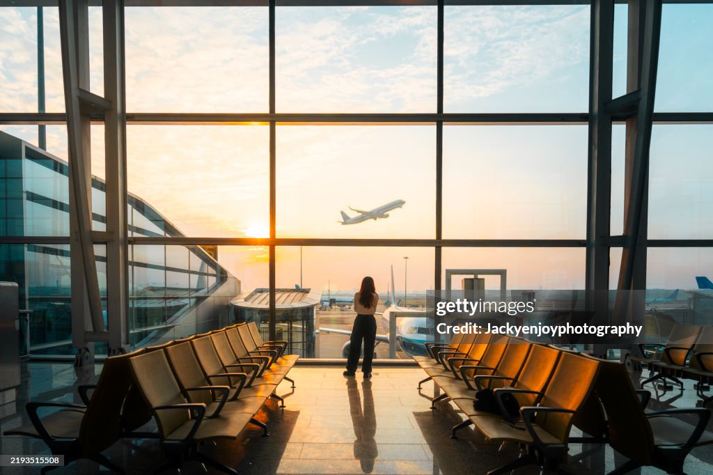 A young Asian woman is using a smartphone to check the arrival departure board and flight schedule at the airport.