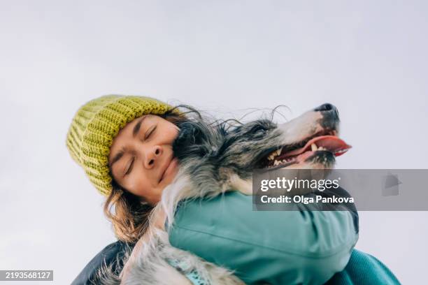 woman wearing a knitted beanie cuddling her border collie dog - lealdade imagens e fotografias de stock