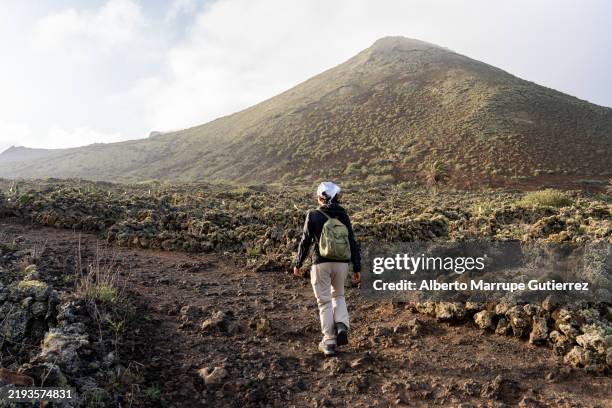 mujer excursionista caminando por un sendero en el paisaje volcánico de lanzarote, islas canarias, españa - lanzarote fotografías e imágenes de stock