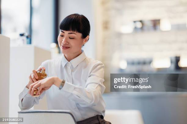 woman testing fragrance in a modern and stylish retail environment - luxury watch stock pictures, royalty-free photos & images