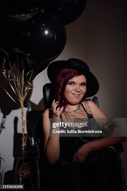 young woman in wheelchair celebrates life with black balloons and stylish outfit in a dimly lit setting - neuromuscular junction stock pictures, royalty-free photos & images