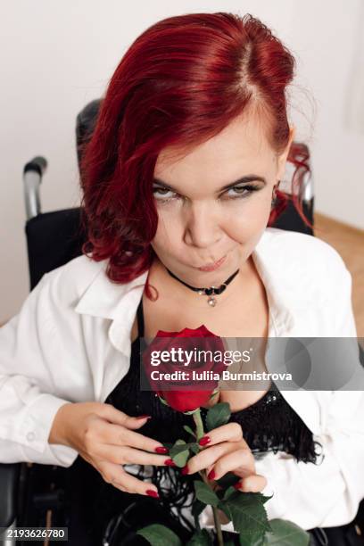 woman in wheelchair holding red rose with vibrant red hair and engaging expression in bright indoor setting - neuromuscular junction stock pictures, royalty-free photos & images