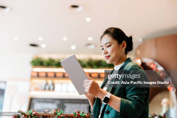 low angle shot of asian businesswoman standing and using digital tablet in hotel cafe. enjoying a relaxing moment in the afternoon. coffee break. lifestyle and technology. green series. - afternoon coffee stock pictures, royalty-free photos & images