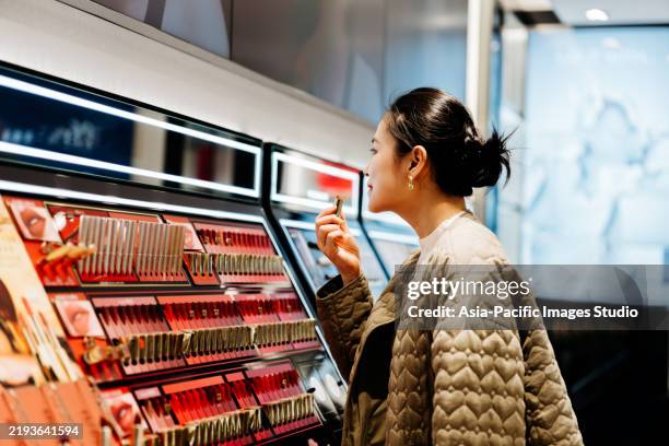 asian beautiful women trying on lipsticks while shopping makeup products at beauty store. - maquilhagem imagens e fotografias de stock
