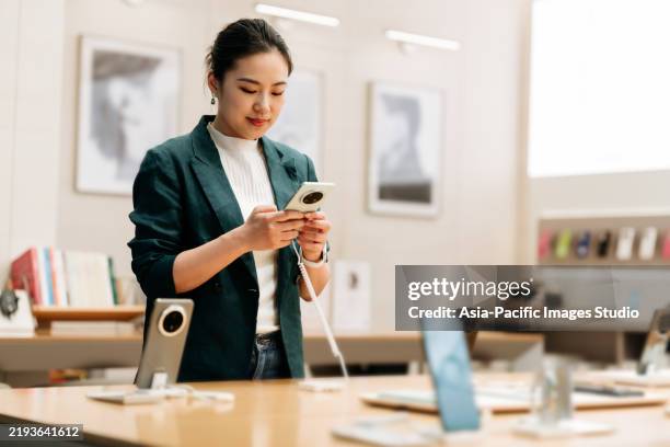 asian businesswoman using and selecting smartphone in modern electronics store. - appliance store stock pictures, royalty-free photos & images