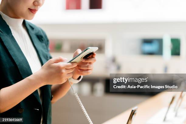 close up of asian businesswoman using and selecting smartphone in modern electronics store. - elektrogeschäft stock-fotos und bilder