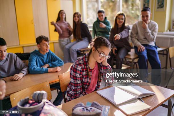 ein mädchen liest, während sich andere kinder im klassenzimmer über sie lustig machen - veralbern stock-fotos und bilder