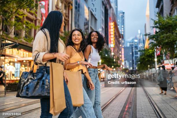 drei junge freundinnen, die spazieren gehen, während tragende einkaufstüten auf der straße in sydney in australien - einkaufen stock-fotos und bilder
