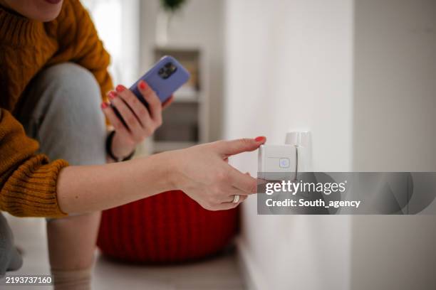 une femme férue de technologie utilise son téléphone près d’une prise murale intelligente. - prise électrique photos et images de collection