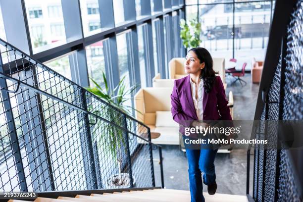 confident businesswoman walking up modern office staircase and looking out window - a escada do sucesso imagens e fotografias de stock