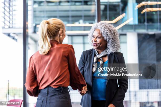 female business colleagues shaking hands in modern business lobby - women shake hands stock pictures, royalty-free photos & images