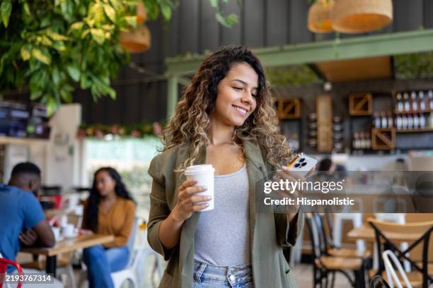 woman leaving a cafe with a coffee to go while using her cell phone - serving food and drinks photos stock pictures, royalty-free photos & images