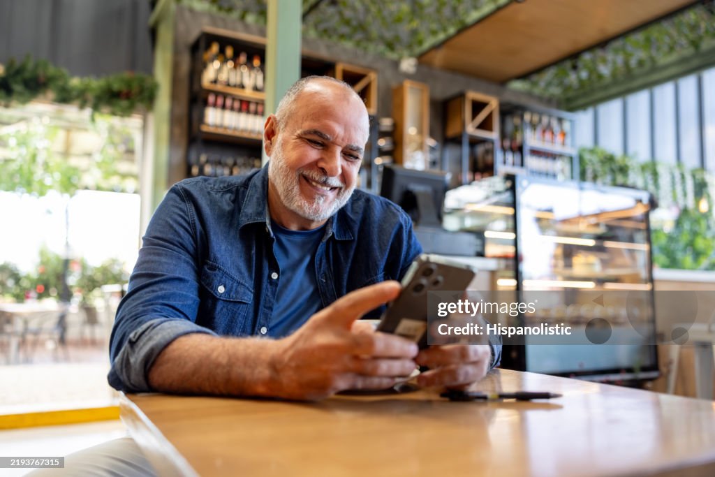 Happy man using his cell phone and smiling at a cafe