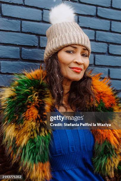 woman stands confidently against a blue wall - fur coat stock pictures, royalty-free photos & images