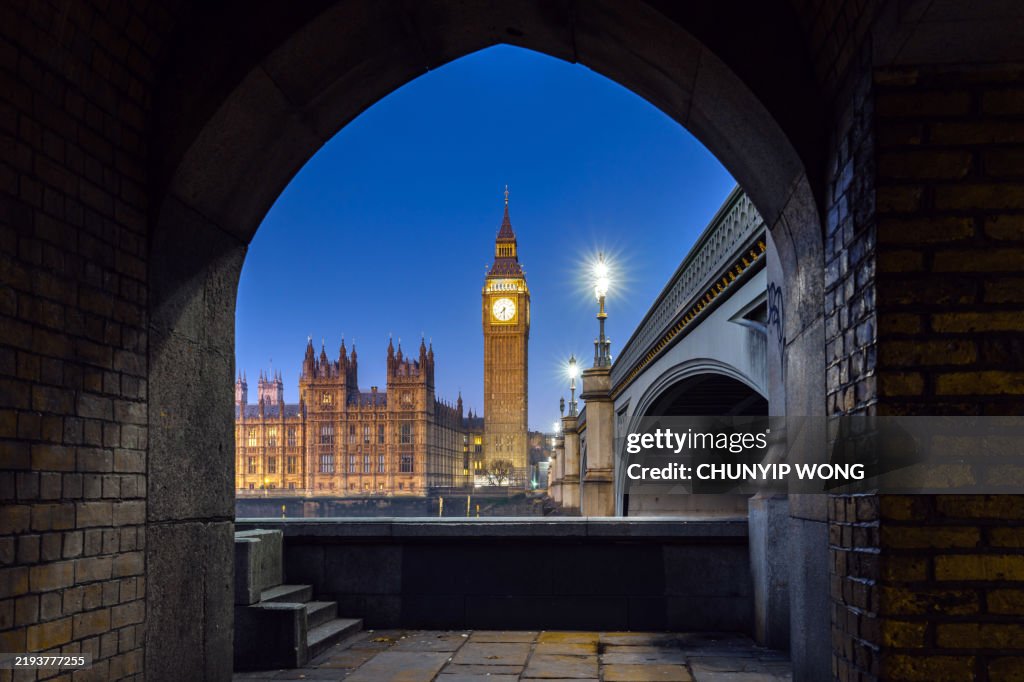 Big ben and houses of parliament emerging from brick archway at twilight