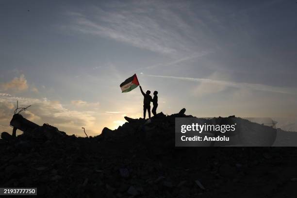 Children hold a Palestinian flag as they stand on rubble while Palestinians in the Bureij Refugee Camp, strive to maintain their routines under...