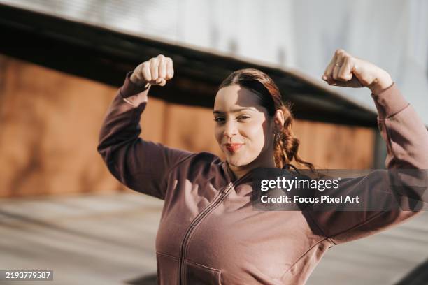 curvy sportswoman flexing biceps after outdoor training, promoting body positivity and healthy lifestyle - voluptuoso fotografías e imágenes de stock